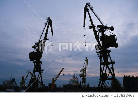 Silhouettes of industrial cranes against the evening sky in a port area. Construction industry. 133628462
