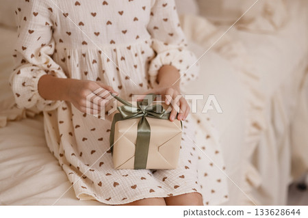Caucasian child hands opening gift box on beige bed in cozy room 133628644
