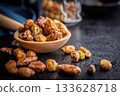 Nuts coated in sugar glaze on wooden spoon on black table. 133628718