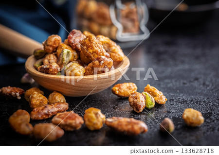 Nuts coated in sugar glaze on wooden spoon on black table. Nuts coated in sugar glaze on wooden spoon on black table. 133628718