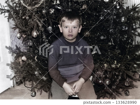A Vintage portrait of a six-year-old boy by the Christmas tree. Retro photo from 1972. A Vintage portrait of a six-year-old boy by the Christmas tree. Retro photo from 1972. 133628990