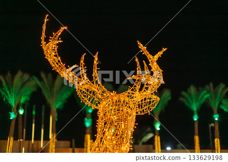 Illuminated deer sculpture with palm trees at night 133629198