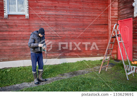 Preparing an electric drill for outdoor installation work, man in warm clothing replaces drill bit in chuck. 133629691