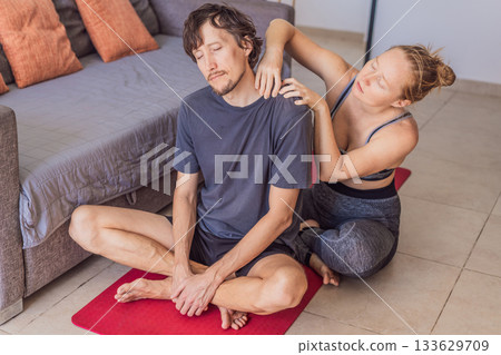 Woman massaging a man's neck on a yoga mat at home, relieving tension and supporting his wellness. Caring touch, relaxation, recovery and healthy lifestyle concept in a peaceful indoor environment Woman massaging a man's neck on a yoga mat at home, relieving tension and supporting his wellness. Caring touch, relaxation, recovery and healthy lifestyle concept in a peaceful indoor environment 133629709