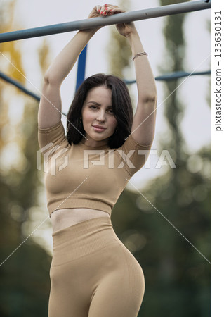 girl engages in physical activity on a sports ground during a sunny afternoon. She hangs from a bar showcasing her strength and focus while enjoying the outdoors. girl engages in physical activity on a sports ground during a sunny afternoon. She hangs from a bar showcasing her strength and focus while enjoying the outdoors. 133630131