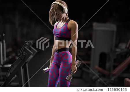 girl wearing bright workout clothes does bicep curls with shiny dumbbells in a modern gym. The atmosphere is focused and energetic highlighting her dedication to fitness. girl wearing bright workout clothes does bicep curls with shiny dumbbells in a modern gym. The atmosphere is focused and energetic highlighting her dedication to fitness. 133630153