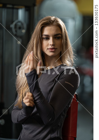 dedicated athlete prepares for a workout in a modern gym environment. She exhibits a determined expression while adjusting her hair. The background shows gym equipment. dedicated athlete prepares for a workout in a modern gym environment. She exhibits a determined expression while adjusting her hair. The background shows gym equipment. 133630175