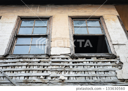 Weathered old building with broken windows and worn wooden lattice on rustic wall Weathered old building with broken windows and worn wooden lattice on rustic wall 133630560