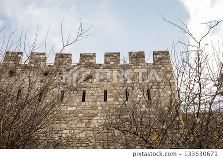 Ancient stone castle wall with battlements against blue sky 133630671