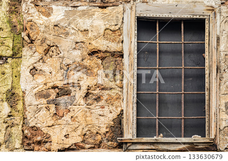 Rustic stone wall with weathered wooden window frame and iron grid bars 133630679