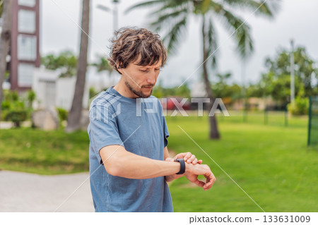 Man checking his sports watch during outdoor workout in the park, tracking progress and performance. Concept of fitness, wellness, active lifestyle, health monitoring, and motivation 133631009