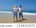 Joyful couple playing at the water's edge on a sunny beach, dressed in casual jeans and white tshirts 133631072