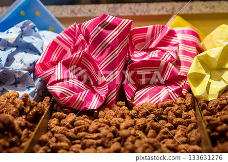 A tray filled with candied nuts at a christmas market stall, surrounded by colorful paper bags ready for serving. A tray filled with candied nuts at a christmas market stall, surrounded by colorful paper bags ready for serving. 133631276