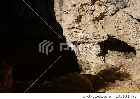 Sunlit cave entrance with rocky terrain 133631452