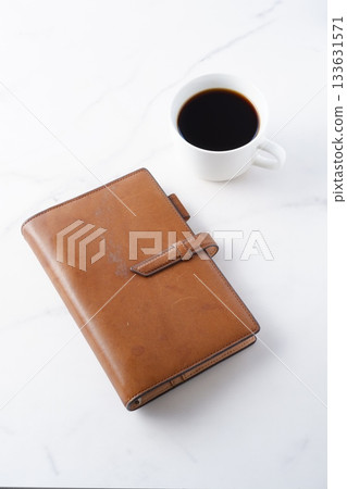 咖啡和記事本-一位男士一邊喝咖啡,一邊在辦公桌前使用棕色皮質記事本工作。 咖啡和記事本-一位男士一邊喝咖啡,一邊在辦公桌前使用棕色皮質記事本工作。 133631571