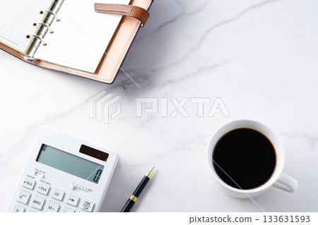 Image of a man doing desk work with a calculator and a personal organizer while drinking freshly brewed coffee Image of a man doing desk work with a calculator and a personal organizer while drinking freshly brewed coffee 133631593