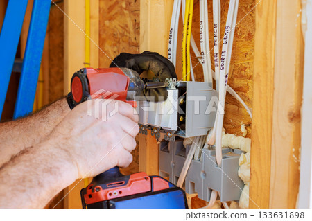Skilled electrician connects electrical wires while installing junction box in newly built structure. Skilled electrician connects electrical wires while installing junction box in newly built structure. 133631898