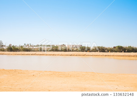 Desert landscape with water and distant buildings Desert landscape with water and distant buildings 133632148