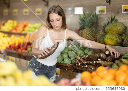 Girl shopping in grocery supermarket - choosing yucca root Girl shopping in grocery supermarket - choosing yucca root 133632980