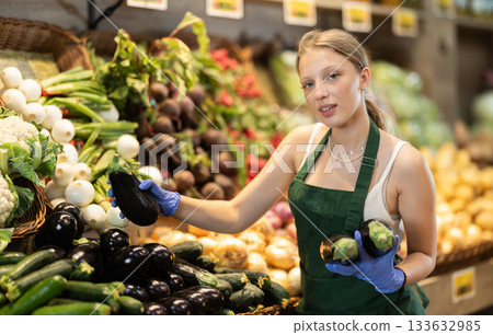 saleswoman lays eggplants on a shelf saleswoman lays eggplants on a shelf 133632985