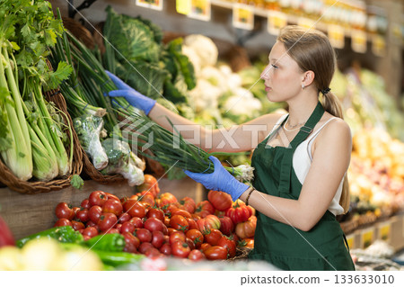 Supermarket employee carefully places green onion on shelves of grocery supermarket 133633010