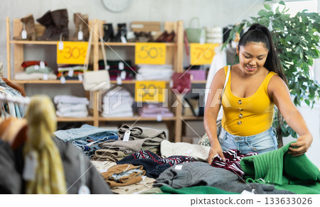 Young woman chooses fashionable sweater in clothing store Young woman chooses fashionable sweater in clothing store 133633026
