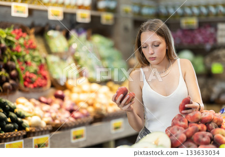 Focused woman shopping in organic food store, choosing flat peaches 133633034