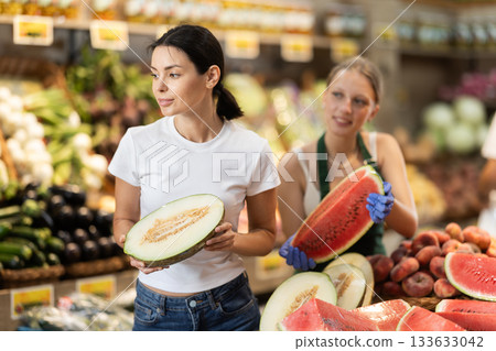 Girl chooses ripe melon in supermarket. Female salesperson offers to choose watermelon 133633042