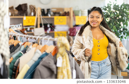 Positive woman tries on a fashionable fur coat in fashionable clothing store 133633046