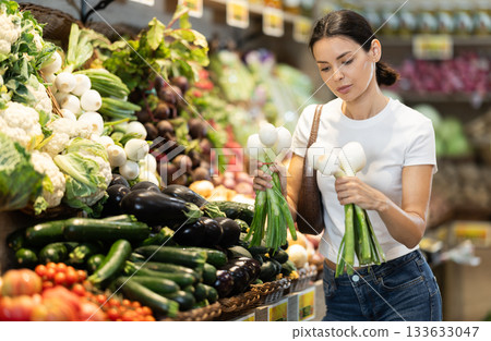 woman chooses a large onion with green stems 133633047