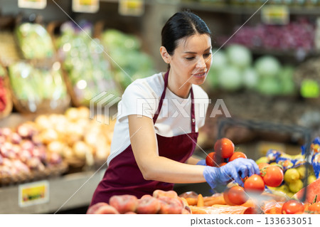 Supermarket employee carefully places ripe tomatoes on shelves of grocery supermarket 133633051
