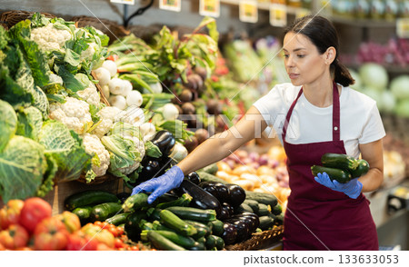 Adult woman seller puts zucchini in vegetable shop Adult woman seller puts zucchini in vegetable shop 133633053