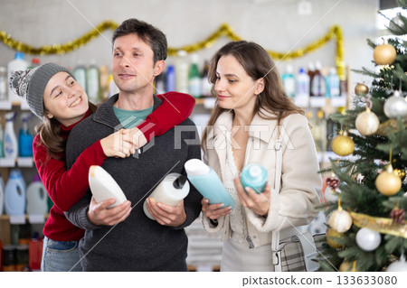 Father, mother and daughter choose shampoo or shower gel in supermarket 133633080