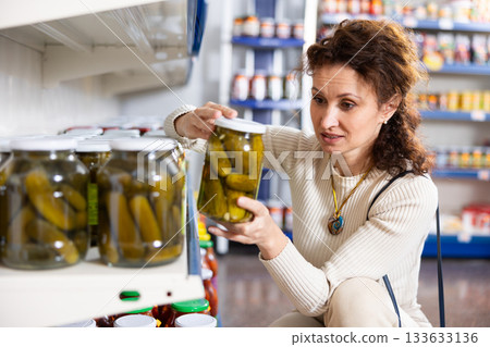 Portrait of woman buying canned cucumbers at grocery store 133633136
