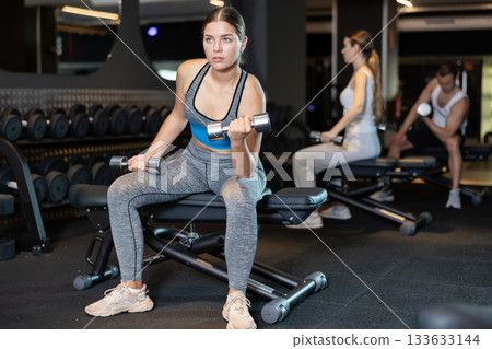 Determined young woman working out with dumbbell in sports hall 133633144