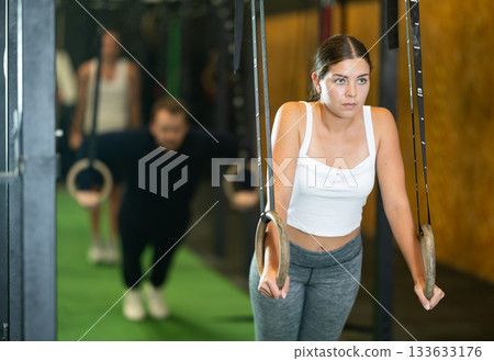 Young woman doing press-ups on gymnastic rings at gym Young woman doing press-ups on gymnastic rings at gym 133633176