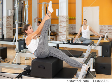 Girl performing exercises on Pilates reformer with sitting box Girl performing exercises on Pilates reformer with sitting box 133633180