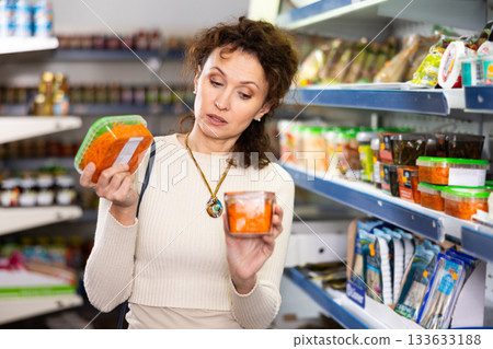 In Russian goods store, woman choose package of pickled Korean spicy carrot salad 133633188