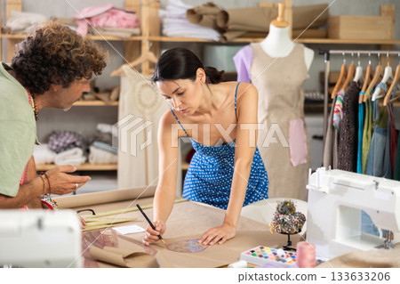 Female and male dressmakers drawing on paper in sewing studio Female and male dressmakers drawing on paper in sewing studio 133633206