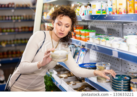 Adult woman chooses pickled herring in store 133633221