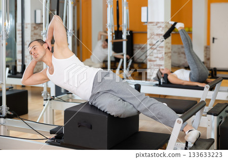 Man in different poses performs static and dynamic exercises on reformer 133633223
