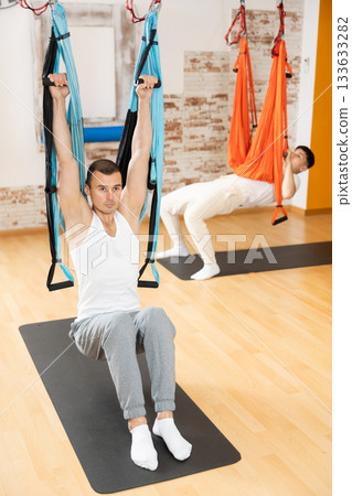 Man visitor performs exercises in hanging position on Pilates slings hammock Man visitor performs exercises in hanging position on Pilates slings hammock 133633282