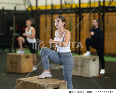 Sportive young girl doing step-up exercises with box during crossfit workout Sportive young girl doing step-up exercises with box during crossfit workout 133633316