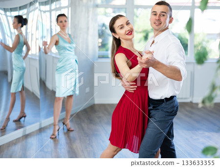 Man practicing samba with female partner in red in dance class Man practicing samba with female partner in red in dance class 133633355