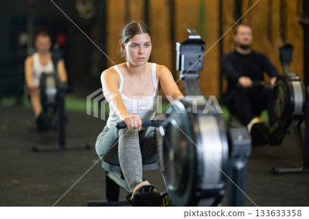 Sporty girl working out on rowing machine during functional training Sporty girl working out on rowing machine during functional training 133633358