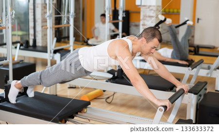 Man in different poses performs static and dynamic exercises on reformer Man in different poses performs static and dynamic exercises on reformer 133633372