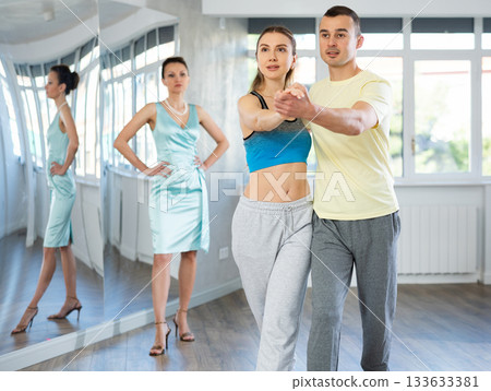 Couple in comfortable sports clothes waltz dancing during individual lesson Couple in comfortable sports clothes waltz dancing during individual lesson 133633381