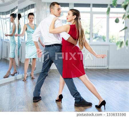 Couple in stage costumes learns tango dancing during individual lesson 133633390