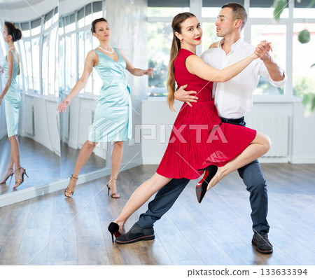 Couple in stage costumes learns tango dancing during individual lesson 133633394