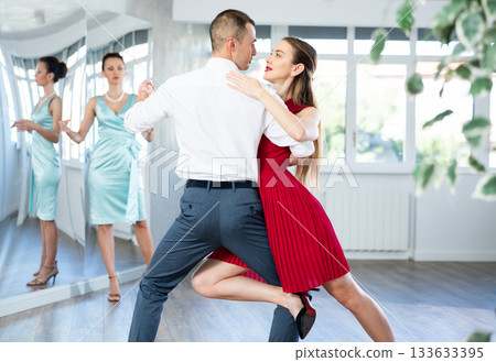 Couple in stage costumes learns tango dancing during individual lesson 133633395